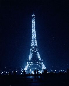 the eiffel tower lit up at night with people standing in front of it