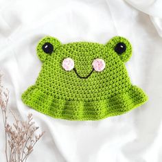 a green crocheted frog hat with eyes and nose on top of a white sheet