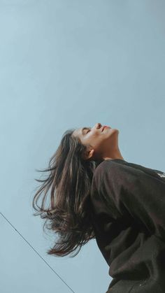 a woman looking up at the sky with her hair blowing in the wind while holding onto an electrical wire