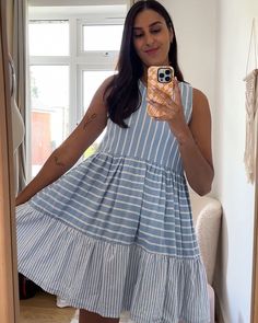 a woman taking a selfie with her cell phone in front of the mirror while wearing a blue and white striped dress