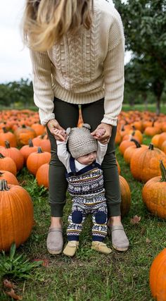 a woman and child standing in front of pumpkins