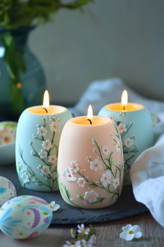 three candles sitting on top of a table next to an egg and flower vases