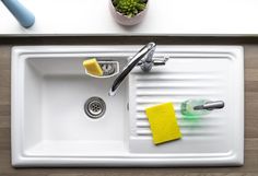 a white sink with yellow sponges on it and a green plant in the corner