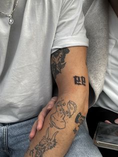 a man with a tattoo on his arm sitting next to another person holding a cell phone