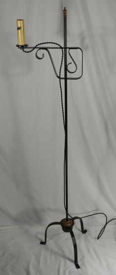 an iron and glass floor lamp with a candle on the base, standing upright against a white backdrop