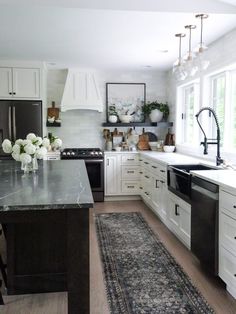 a kitchen with white cabinets and black counter tops, an area rug on the floor