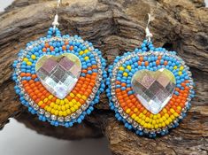 a pair of colorful beaded earrings on top of a tree branch with a rock in the background