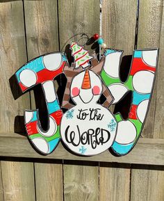 a wooden sign that says joy to the world hanging on a fence with christmas decorations