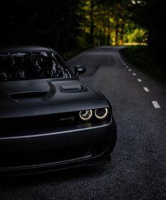 the front end of a black sports car on a dark road with trees in the background