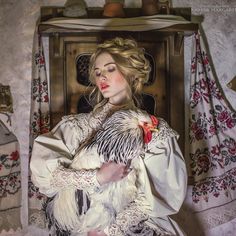 a woman is holding a chicken in her arms and posing for the camera with an ornate background