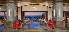 a lobby with chairs and chandeliers overlooking the ocean at sunset or dawn,