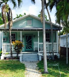 a small blue house with palm trees in the front yard and walkway leading up to it