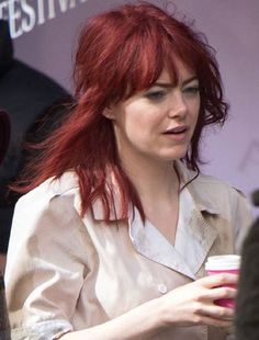 a woman with red hair is holding a cup in her hand and talking to someone