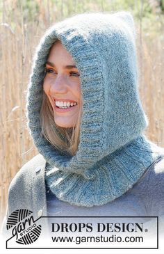 a woman wearing a hood and smiling for the camera in front of some tall grass