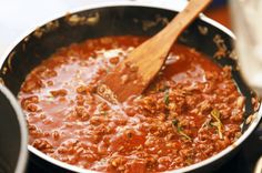 a wooden spoon in a pot filled with chili and meat sauce on top of a stove