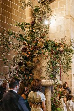 a group of people standing next to each other in front of a stone pillar with flowers on it