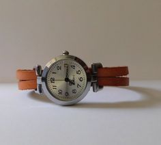 This is a simple women watch with a leather flat cord strap. The style is retro minimalist with a simple distress look. The face of the watch is made in silvered finish alloy, free of nickel and lead, round shape 1 inch diameter. The strap comes in 6 sizes: XS for a 6.00 inches wrist S for a 6.25 inches wrist M for a 6.50 inches wrist L for a 6.75 inches wrist XL for a 7.00 inches wrist XXL for a 7.25 inches wrist If you need another size, please send me a message. The clasp is magnetic and is m Minimalist Everyday Watch With Adjustable Fit, Leather Watches With Bracelet Strap For Everyday Use, Adjustable Minimalist Watches For Everyday Use, Minimalist Adjustable Watches For Everyday Use, Minimalist Adjustable Everyday Watches, Brown Leather Strap Cuff Watch, Leather Wrist Strap For Watches, Everyday Use, Distressed Brown Leather Watch Strap, Retro Minimalist