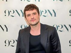 a man standing in front of a wall wearing a black shirt and suit jacket with pinstriped stripes