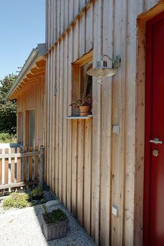 a red door and window in front of a wooden building with a planter on the side