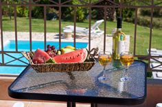 watermelon and grapes in a basket on a table next to a pool