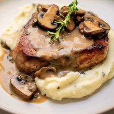 a white plate topped with mashed potatoes covered in mushroom gravy and mushrooms