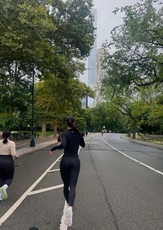 two women running down the street in tight black clothing and white sneakers, with tall buildings in the background