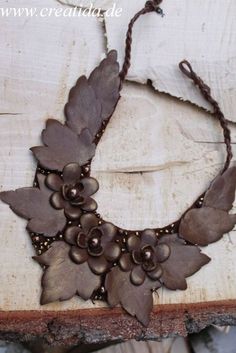 a necklace with leaves and beads is shown on a piece of drift wood that has been painted brown