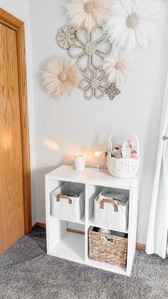 a white shelf with baskets and lights on it in front of a wall decorated with flowers