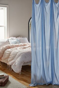 a bed sitting next to a window covered in blue drapes on top of a wooden floor