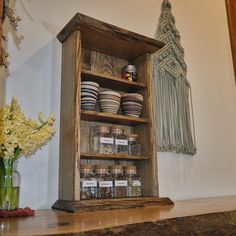 a wooden shelf filled with lots of dishes on top of a counter next to a vase