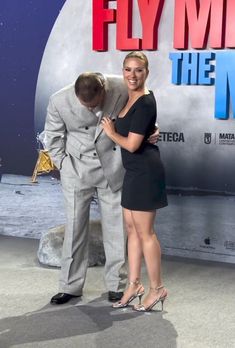 a man and woman standing next to each other in front of a sign that says fly me the moon