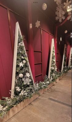 christmas trees are lined up in front of red walls with snowflakes on them