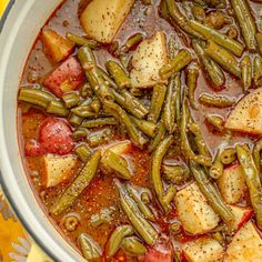 a pot full of stew with potatoes and green beans in it on a yellow table cloth