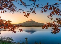 the sun is setting over a lake with trees in front of it and a mountain in the distance