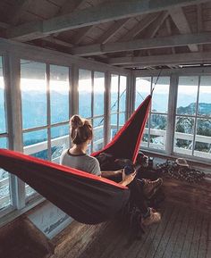 a woman is sitting in a hammock looking out the window at the ocean