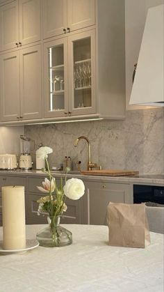 a kitchen with marble counter tops and white flowers in a glass vase on the table