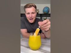 a man holding a straw in front of a glass filled with orange juice