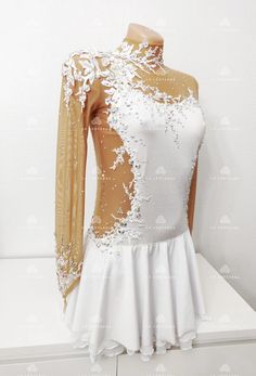 a white dress with gold trim and sequins on the shoulders is displayed in front of a white wall