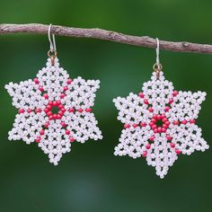 two white and red beaded earrings hanging from a tree branch