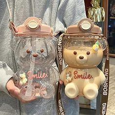 a person holding two clear teddy bears in their hands, one is wearing a pink hat and the other has a smile on it's face