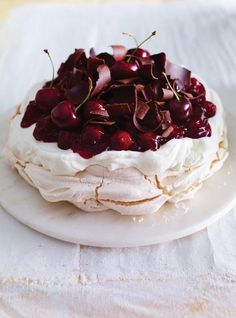 a cake with cherries and whipped cream frosting sitting on a white platter