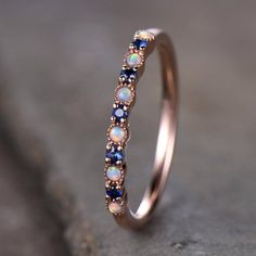 a gold ring with blue and white opal stones on it, sitting on top of a rock