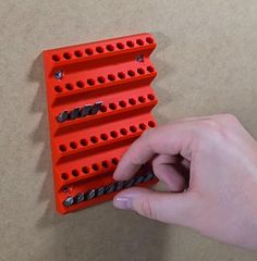 a hand is holding a red piece of plastic that has holes in the middle and screws on it