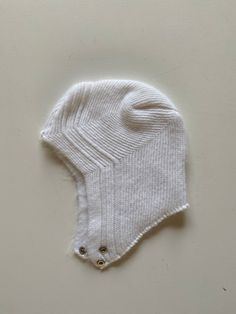 a white knitted hat with buttons on the front and side, sitting on top of a