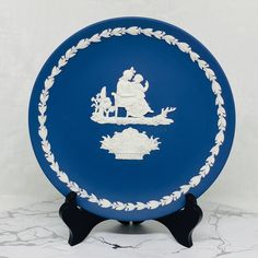 a blue and white plate sitting on top of a black stand next to a wall