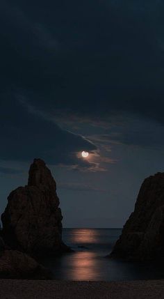 the moon is setting over the ocean and rocks