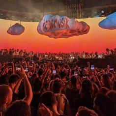 a crowd of people holding up cell phones in front of a stage with an orange sky