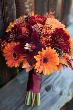 a bridal bouquet with orange and red flowers is sitting on a wooden bench outside