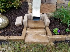 an outdoor toilet in the middle of some grass and flowers next to a rock wall