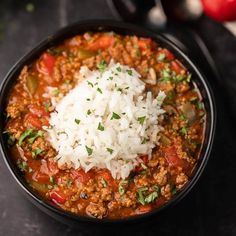 a black bowl filled with chili and rice on top of a table next to an apple